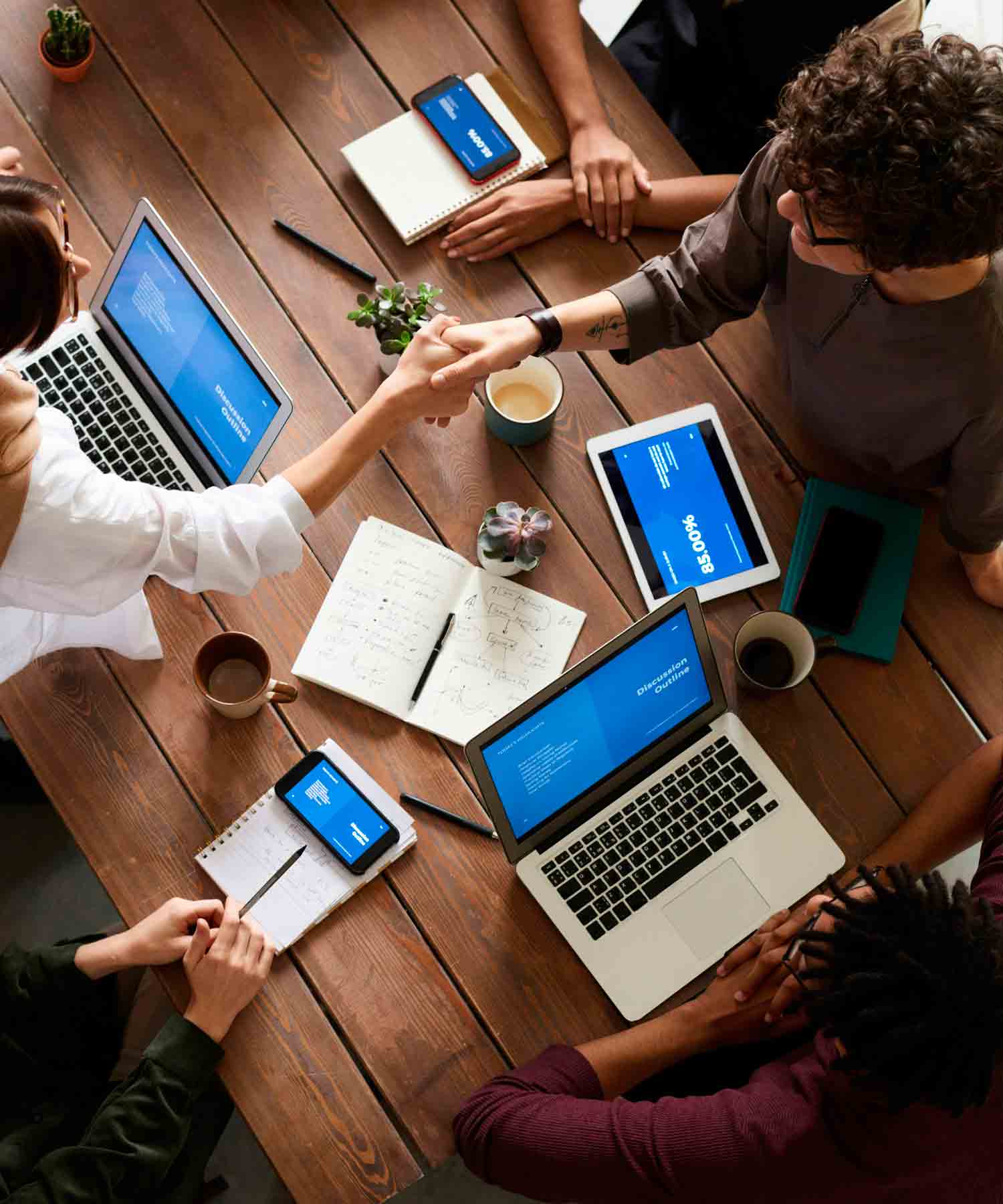 Personas reunidas alrededor de una mesa, con computadores y dándose las manos.